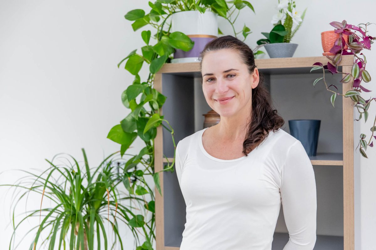 Katka Gazdik, smiling, standing in front of a shelf of houseplants