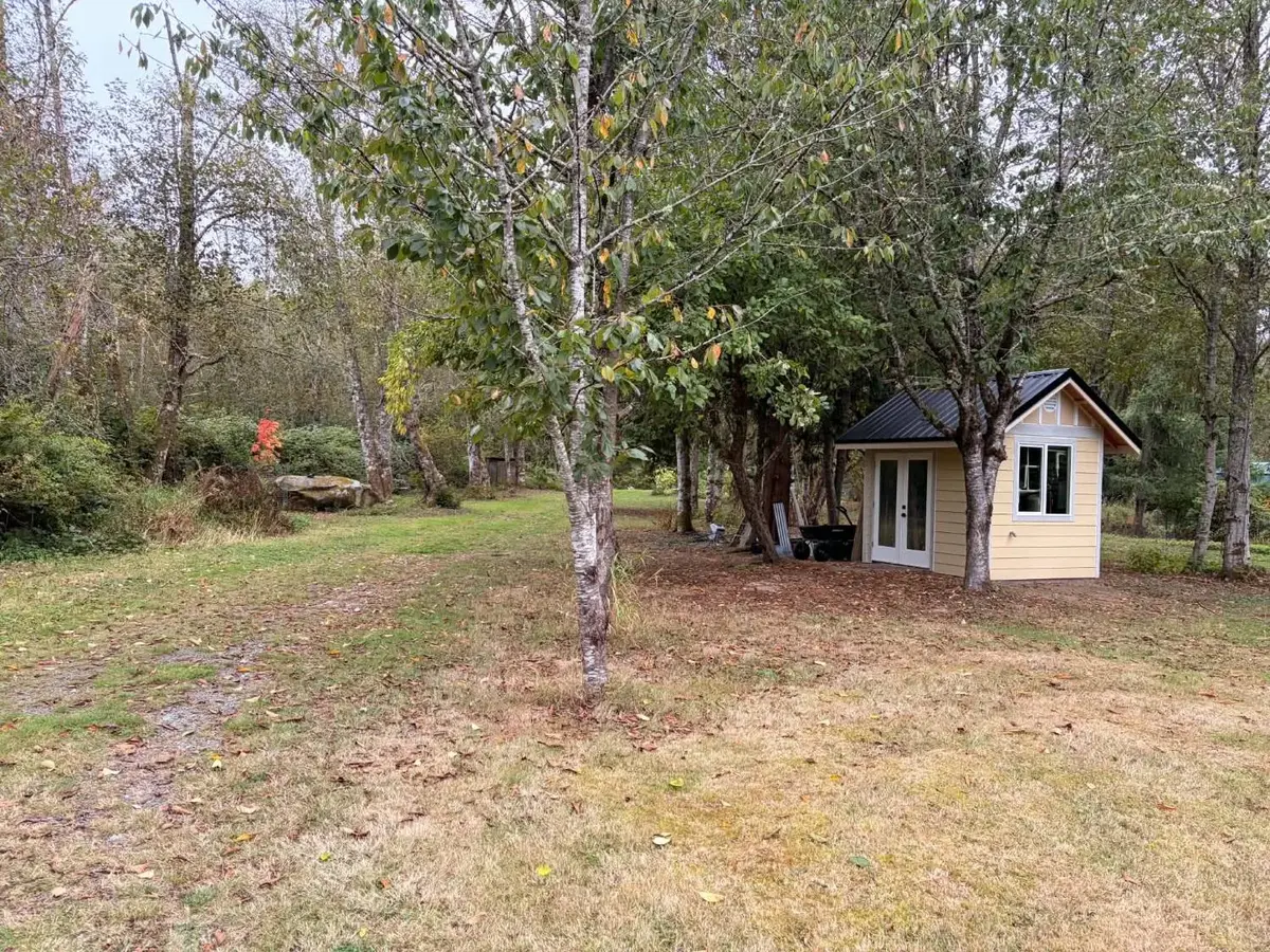 The new pumphouse up close, with pale yellow siding, a black metal roof and white French doors, among the trees